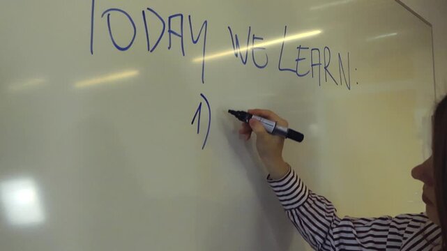 Female professor's hand writing with a blue marker the subject of today's lesson, math, on a whiteboard in a classroom. Educational scene representing knowledge and teaching in school