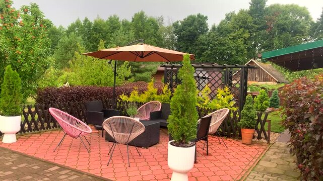 Modern backyard patio featuring stylish pink Acapulco chairs, outdoor umbrella, lush green garden landscaping, and cozy seating area for summer relaxation.