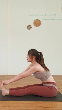 Asian Woman Performing Seated Forward Fold Yoga Stretch in Studio
