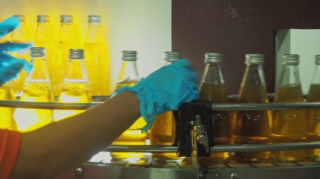 Quality control worker inspecting sealed beverage bottles on an automated conveyor belt in a modern industrial plant, ensuring hygiene, packaging integrity, and food safety standards.