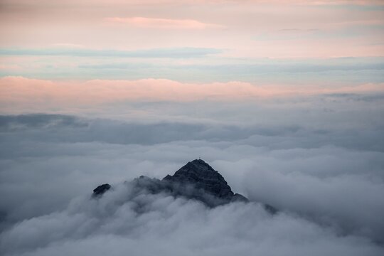 A serene mountain peak emerges gracefully above a thick blanket of rolling clouds during a soft pastel sunrise in the high alpine wilderness