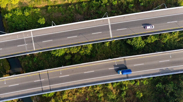 Aerial view of a dual-carriageway highway bridge spanning over lush green vegetation with a car and a truck driving on the asphalt lanes in Boyolali, Central Java, Indonesia.