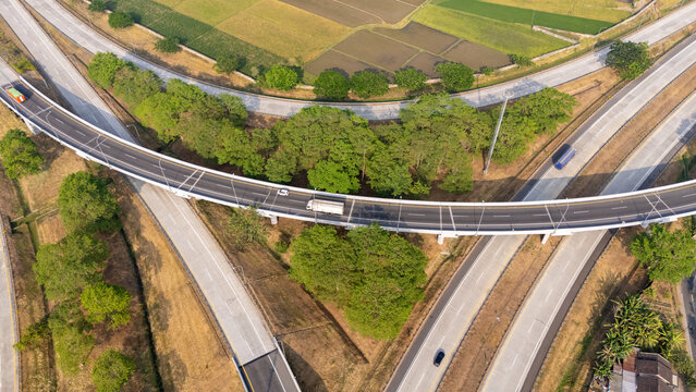 Aerial view of a highway interchange with vehicles driving on the road, surrounded by green trees and agricultural fields in Boyolali, Central Java, Indonesia.