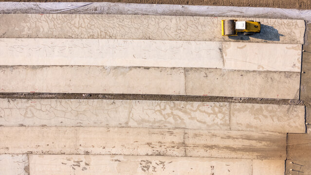 Aerial view of a yellow road roller compacting concrete sections at a construction site in Sleman, Special Region of Yogyakarta, Indonesia.