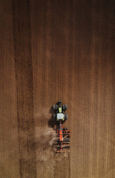 Vertical top-down aerial view of a single heavy tractor and seeder combination moving straight through a vast brown field during spring planting.
