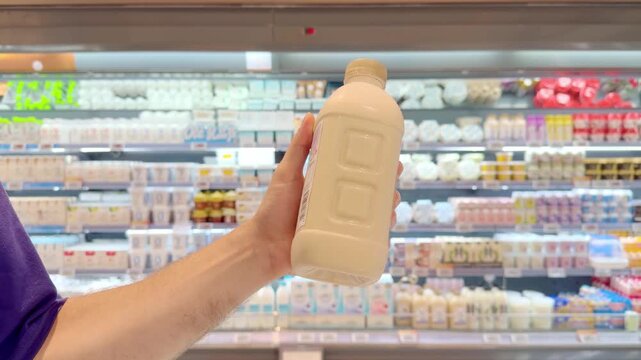 Young Man Reading Labels on Milk, Yogurt and Cheese Bottles in Supermarket Dairy Aisle &ndash; Checking Ingredients and Nutrition Facts Before Buying