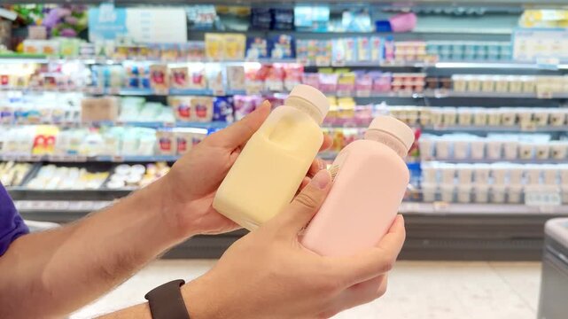 Young Man Reading Labels on Milk, Yogurt and Cheese Bottles in Supermarket Dairy Aisle &ndash; Checking Ingredients and Nutrition Facts Before Buying