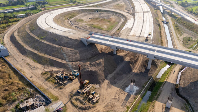 Aerial view of a highway construction site featuring a curved ramp, bridge structure, and heavy machinery in Yogyakarta, Special Region of Yog, Indonesia.