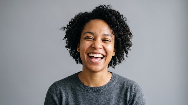 Portrait of a cheerful young woman smiling brightly for a professional identity photo against a minimalist neutral grey background