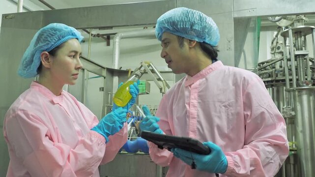 Asian food scientists sterile protective suit inspect bottle beverage quality data digital tablet beside automated production line food safety compliance industrial quality assurance laboratory test 