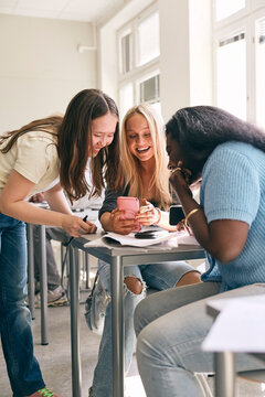 Happy female high school students using smart phone in classroom