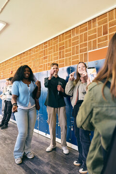 Girl photographing smiling teenage students posing near lockers in school corridor