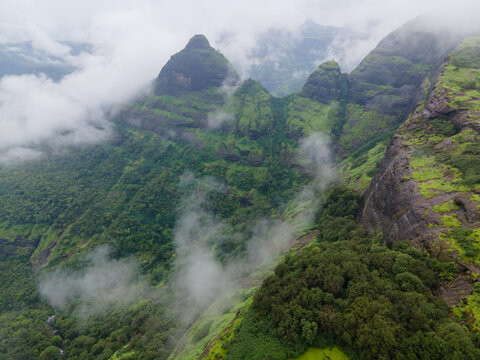 Aerial view of the lush green Western Ghats mountains featuring steep slopes, dense vegetation, and misty clouds rolling over the peaks in Lonavala, Maharashtra, India.