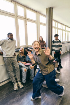 Portrait of happy female teacher photo bombing teenagers photograph in college corridor