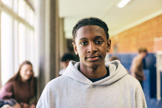 Portrait of teenage male college student wearing hooded shirt standing in corridor