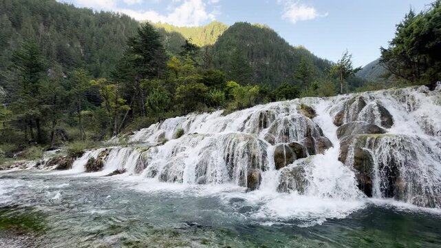 Clear turquoise water cascading over mossy calcified rocks at Double Dragon Lake Waterfall in Jiuzhaigou National Park, Sichuan, China, with dynamic splashes and forest scenery. Shuang Long Hai