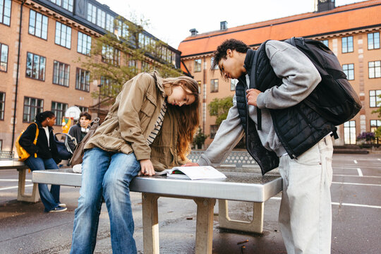 Male and female students studying together on ping pong table in school campus