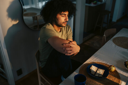 Depressed man hugging his knees while sitting at dining table