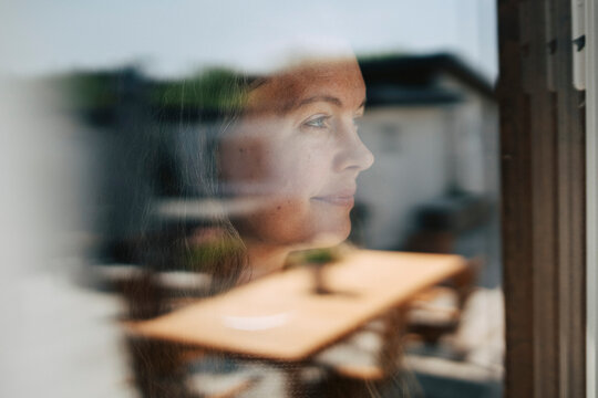 Smiling mature woman looking through glass window
