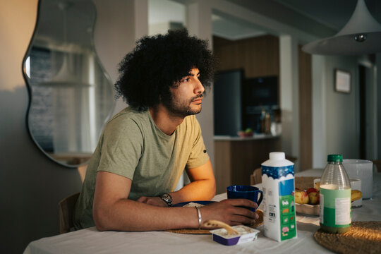 Depressed man with curly hair contemplating while sitting at dining table