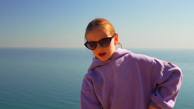 Stylish girl raps confidently by the shimmering ocean while wearing a violet hoodie. Static medium shot capturing expressive hand gestures.