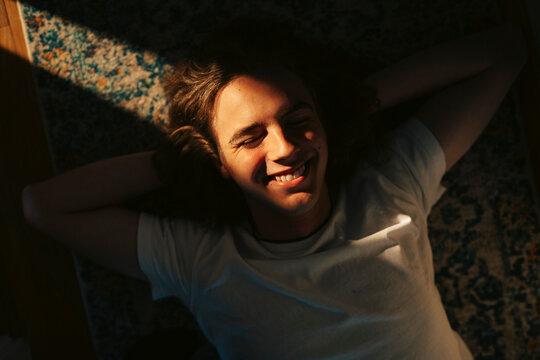 Happy young man lying down with eyes closed at home