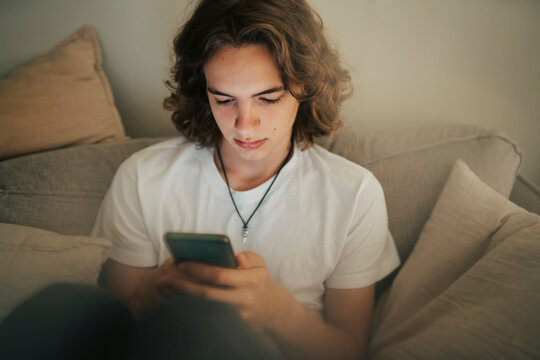 Young man text messaging through smart phone while sitting on sofa at home