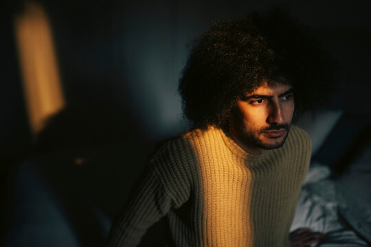 Lonely man with curly hair sitting in bedroom