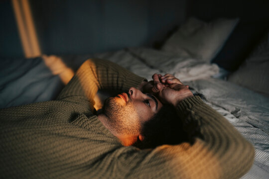 Depressed man lying down on bed at home
