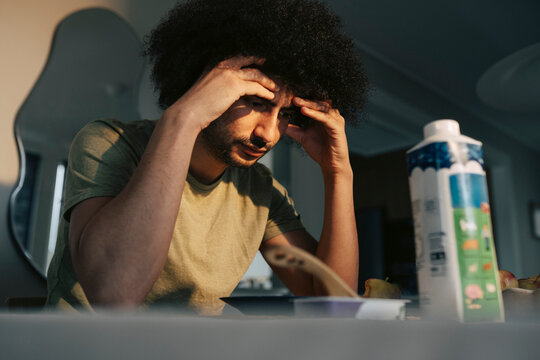 Man with head in hands looking at breakfast plate while sitting at dining table