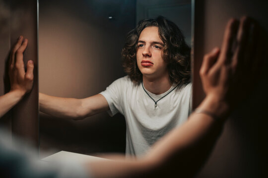 Sad young man looking at reflection in bathroom mirror at home
