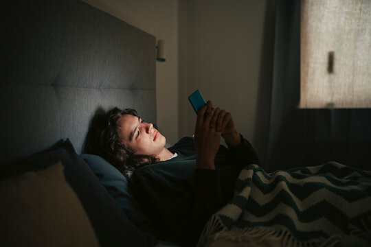 Young man using smart phone while lying down on bed during nighttime
