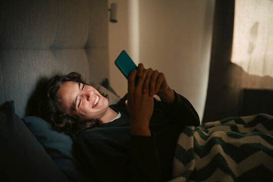 Smiling young man spending leisure time using smart phone at home