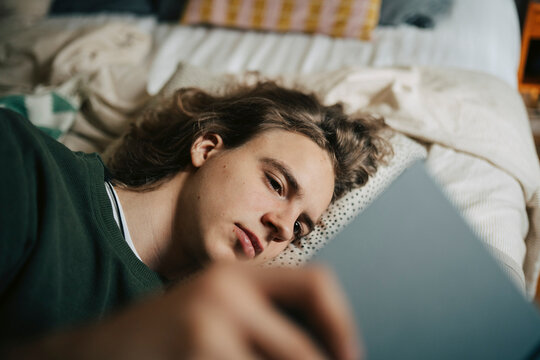 Young man reading book while lying down on bed at home