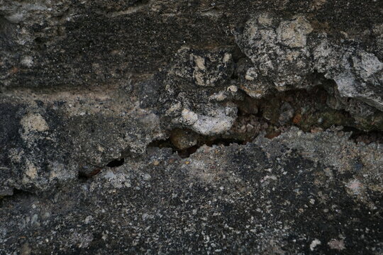 Close-up texture of fractured, weathered concrete revealing a dark structural crevice with crumbling aggregate. The shot conveys concepts of structural fatigue, architectural wear, seismic damage, con