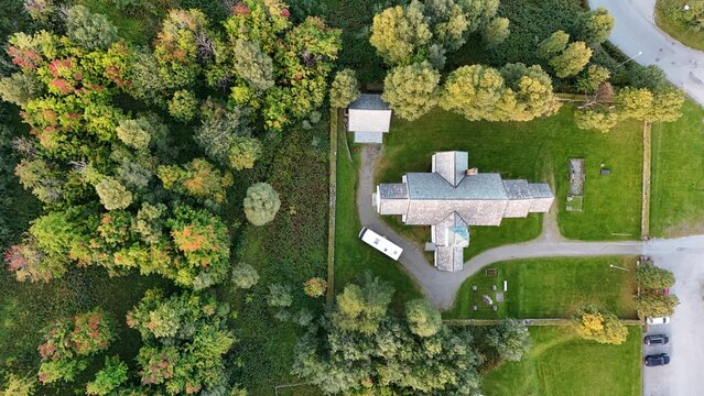 Aerial view of Skjervoy Church surrounded by lush green trees, manicured lawns, and a small parking area in Skjervoy, Troms, Norway.