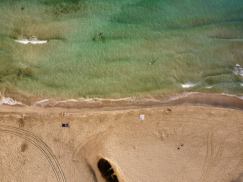 Aerial view of Son Bou beach with clear turquoise water, gentle waves, and tire tracks on the golden sand in Son Bou, Illes Balears, Spain.