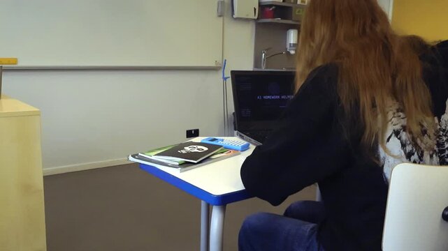 Female student sitting at a desk in a classroom using a laptop with an artificial intelligence homework helper program to find answers, showcasing the future of personalized education