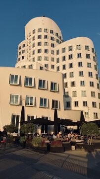 Modern curved white architecture with people riding bicycles and enjoying an outdoor caf&eacute; along a city promenade.