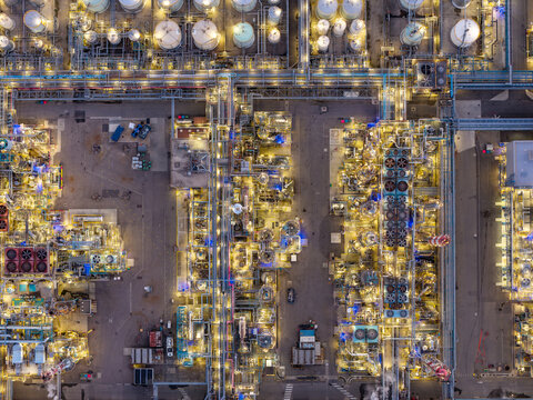 Aerial view of an industrial refinery at night, illuminated by bright lights, featuring complex pipe networks, storage tanks, and processing units in Bantzenheim, Grand Est, France.