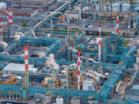 Aerial view of the industrial refinery complex in Bantzenheim, featuring blue pipes, tall red and white chimneys emitting steam, and storage tanks in Bantzenheim, Grand Est, France.