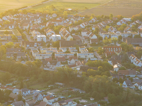 Aerial view of the residential neighborhood of Bantzenheim featuring rows of houses, lush green trees, and quiet streets illuminated by warm golden hour light in Bantzenheim, Grand Est, France.