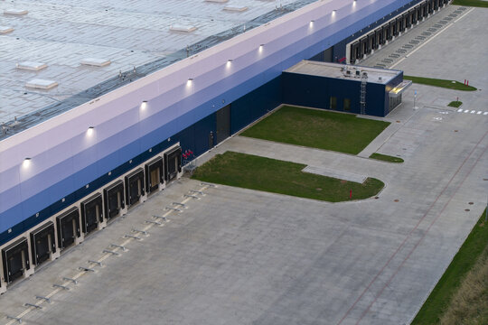 Aerial view of a modern logistics hub and warehouse facility featuring multiple loading docks, a blue and purple gradient facade, and a large concrete yard in Poland.