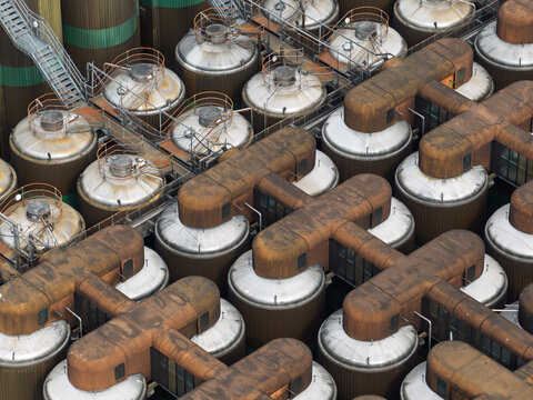Aerial view of a beer brewery featuring numerous large industrial fermentation tanks connected by a complex network of metal pipes and walkways in the United Kingdom.
