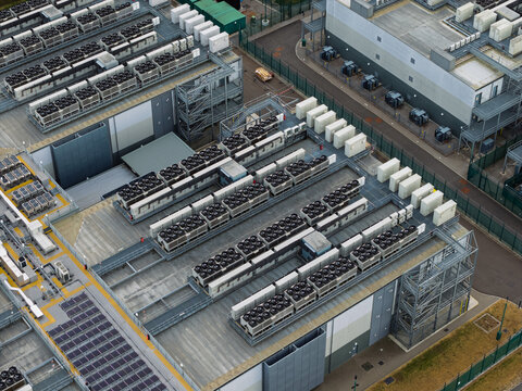 Aerial view of a data center featuring rows of industrial HVAC cooling units on the roof, modern infrastructure, and secure perimeter fencing in the United Kingdom.
