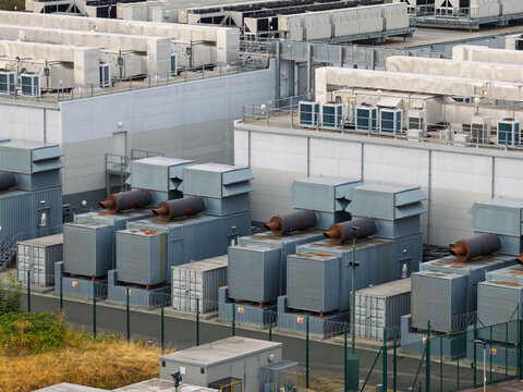 Aerial view of a data center facility featuring rows of industrial cooling units, power generators, and secure perimeter fencing in the United Kingdom.
