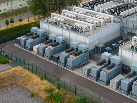 Aerial view of Data Center with rows of industrial cooling units and power generators situated within a fenced facility in United Kingdom.