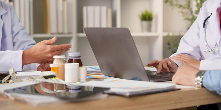Doctors hands typing on laptop during medical consultation with pill bottles on desk