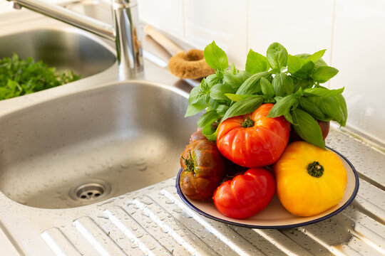 Tomates rouges et jaunes avec du basilic frais empil&eacute;s sur une assiette pos&eacute;e sur un &eacute;vier de cuisine en inox