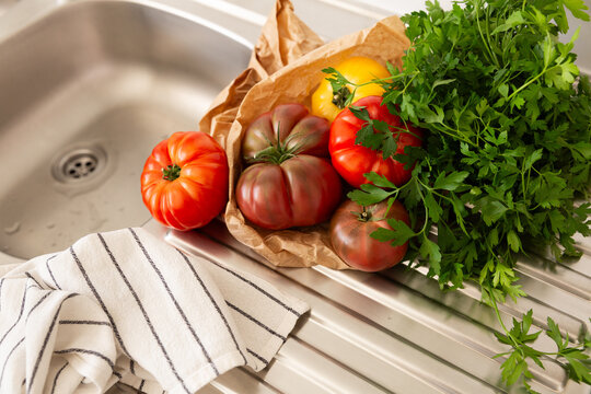 R&eacute;colte de tomates anciennes rouges et jaunes avec du persil frais dans un sac en papier kraft pos&eacute;s sur un &eacute;vier de cuisine en inox